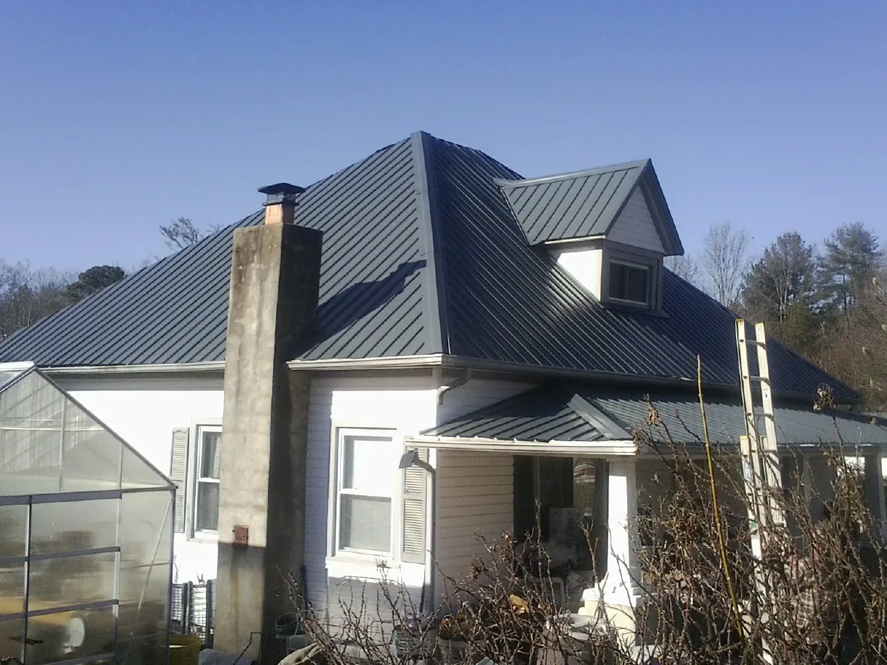 Dark blue standing seam metal roof on a white farmhouse with dormer — Slate & Tile Roof Repair by Roofing Brothers in Earlville